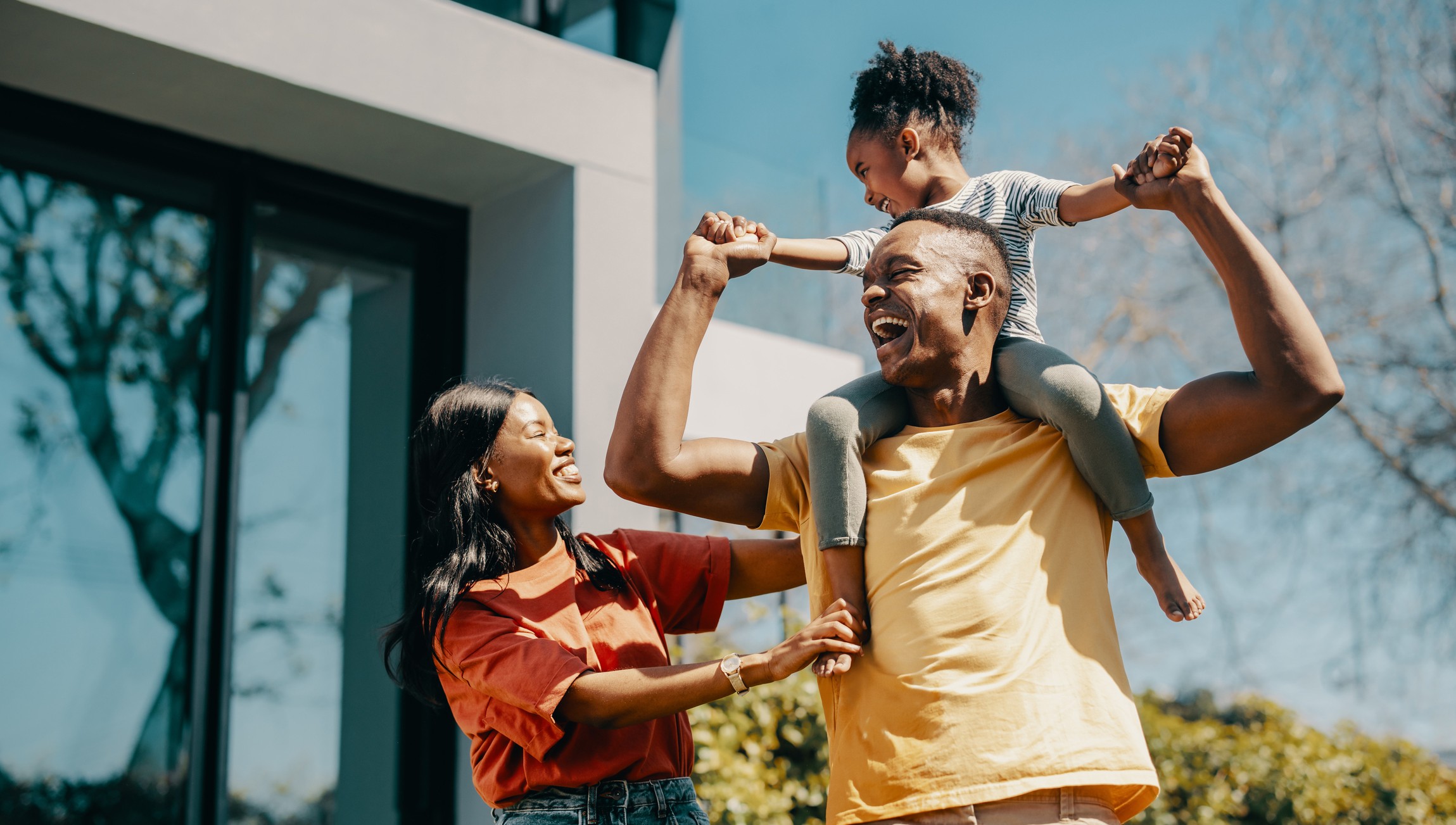 Family fun time with mom and dad at home. Couple playing with their daughter and creating happy childhood memories. Dad carrying his daughter on his shoulders and standing next to mom.