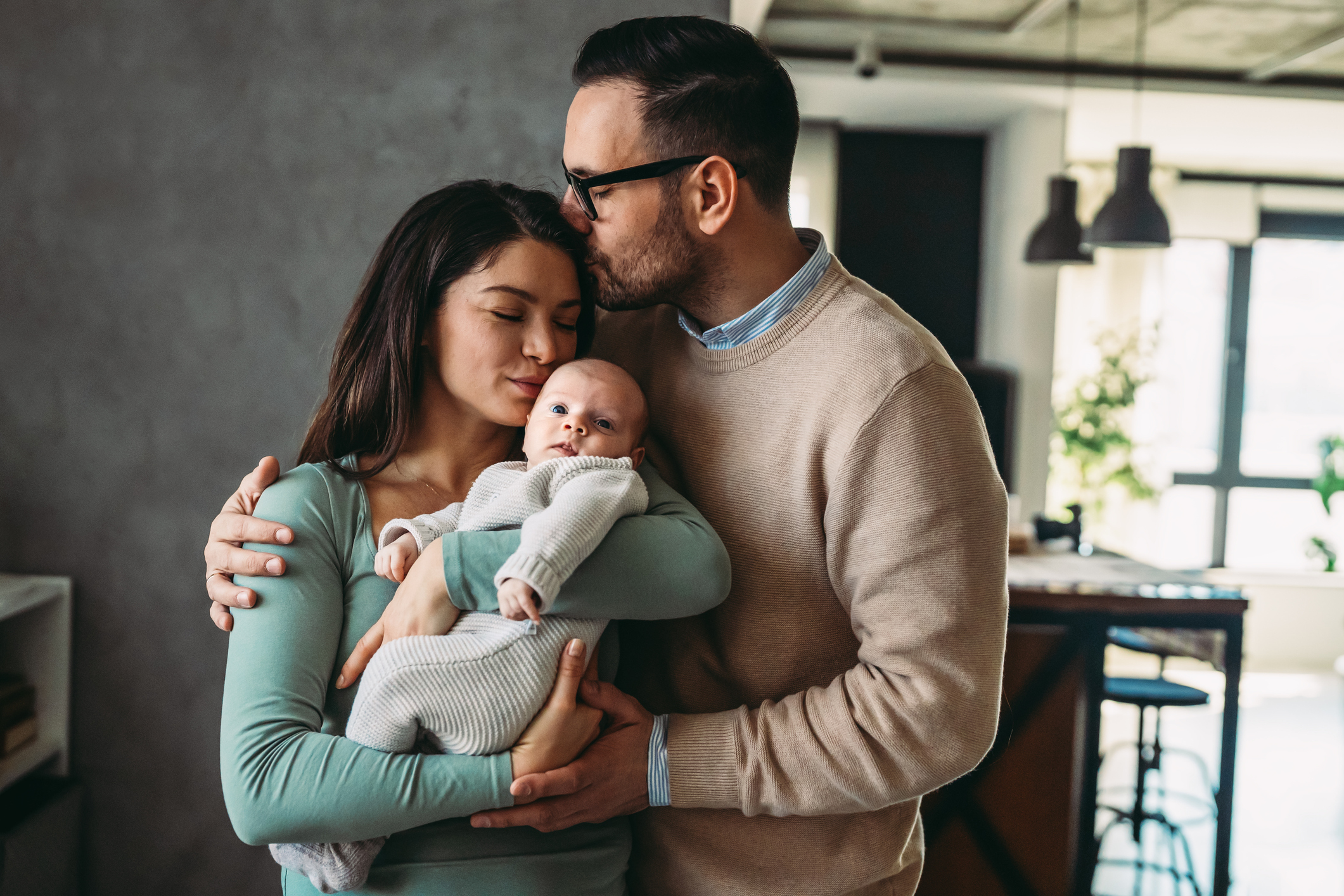 Husband hugging and kissing wife holding their baby
